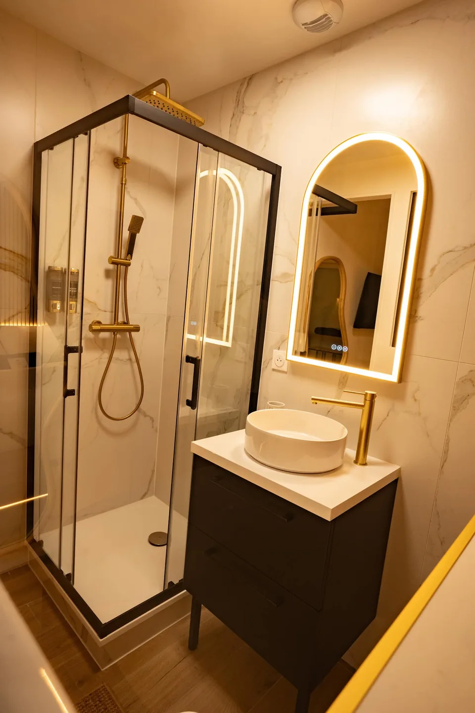 La douche vitrée, la vasque et le miroir éclairé de la salle d'eau