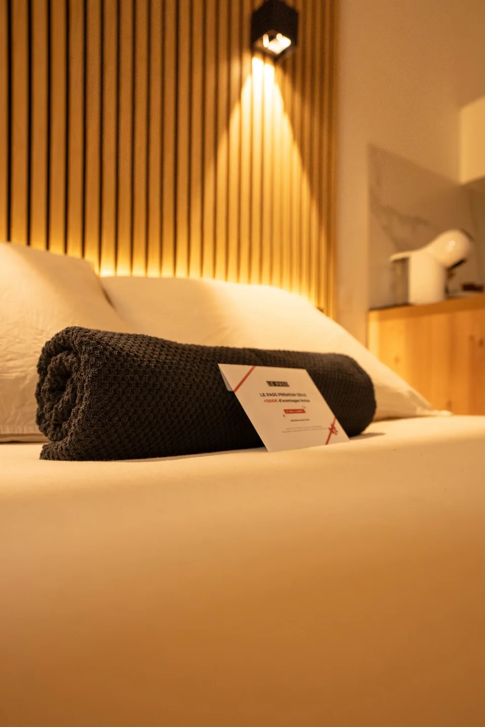 Les serviettes préparées sur le lit, devant la tête de lit en bois éclairée