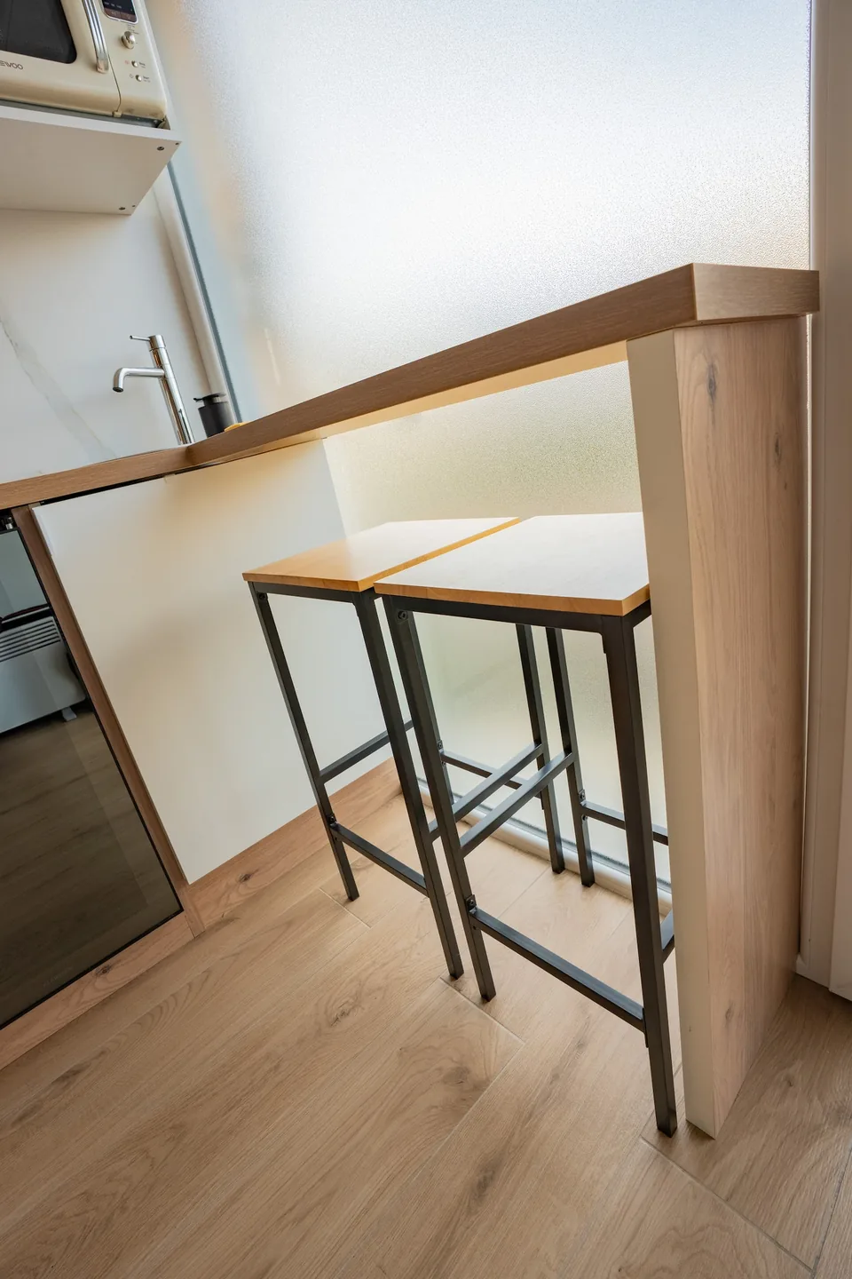 La table haute en bois et ses tabourets près de la fenêtre